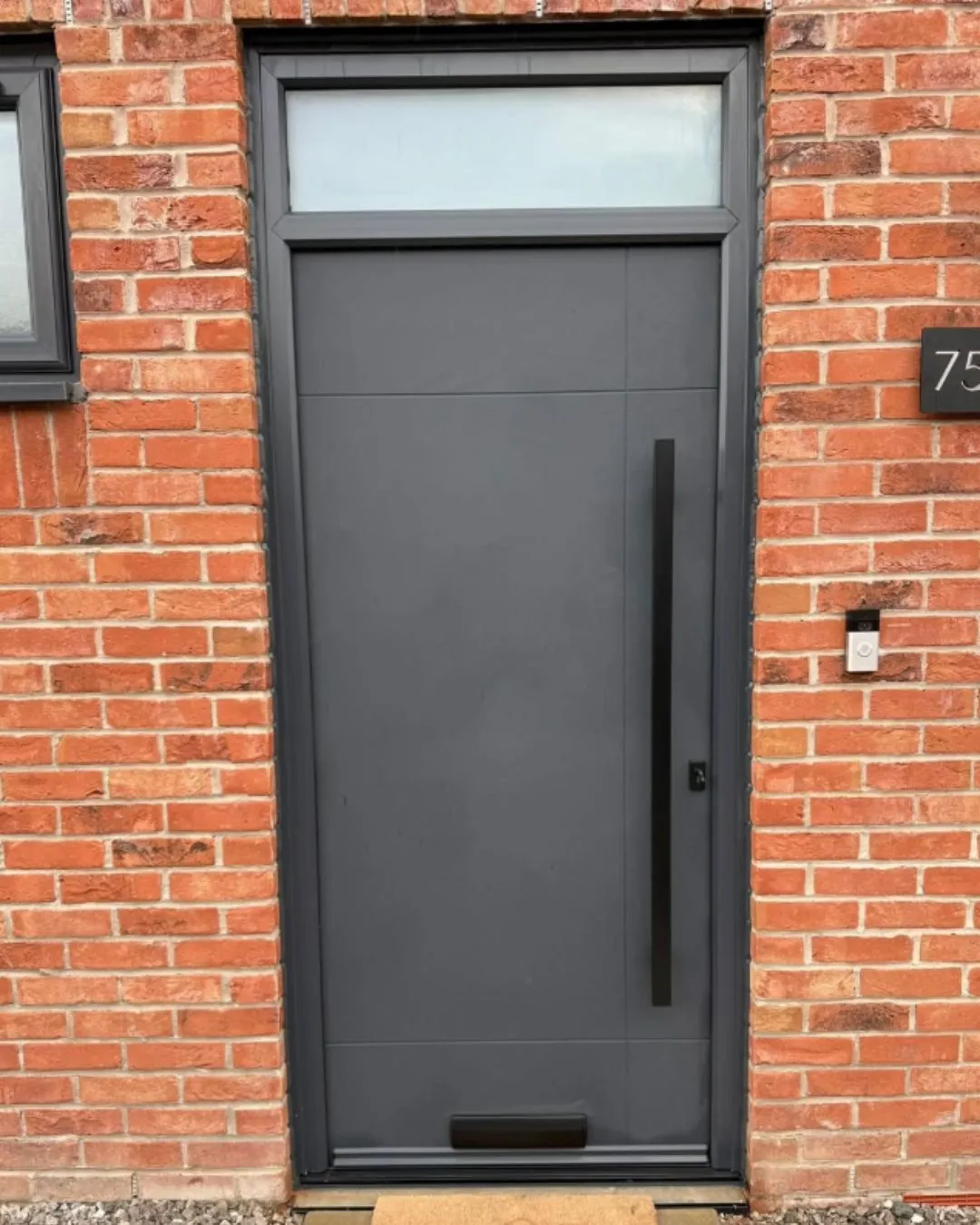 Anthracite grey front door with a matching glazed transom above, set in a red brick wall
