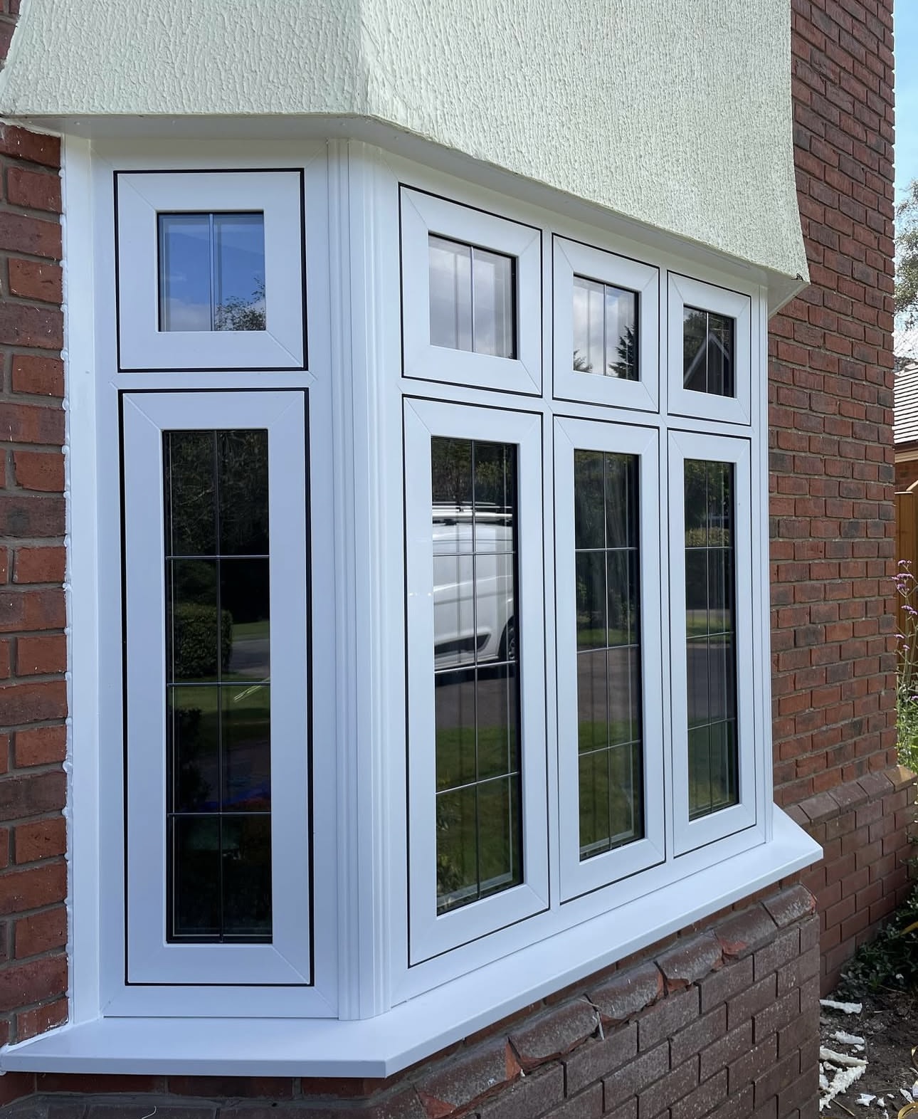White bay window with decorative leaded glass bars on a red brick and cream rendered home