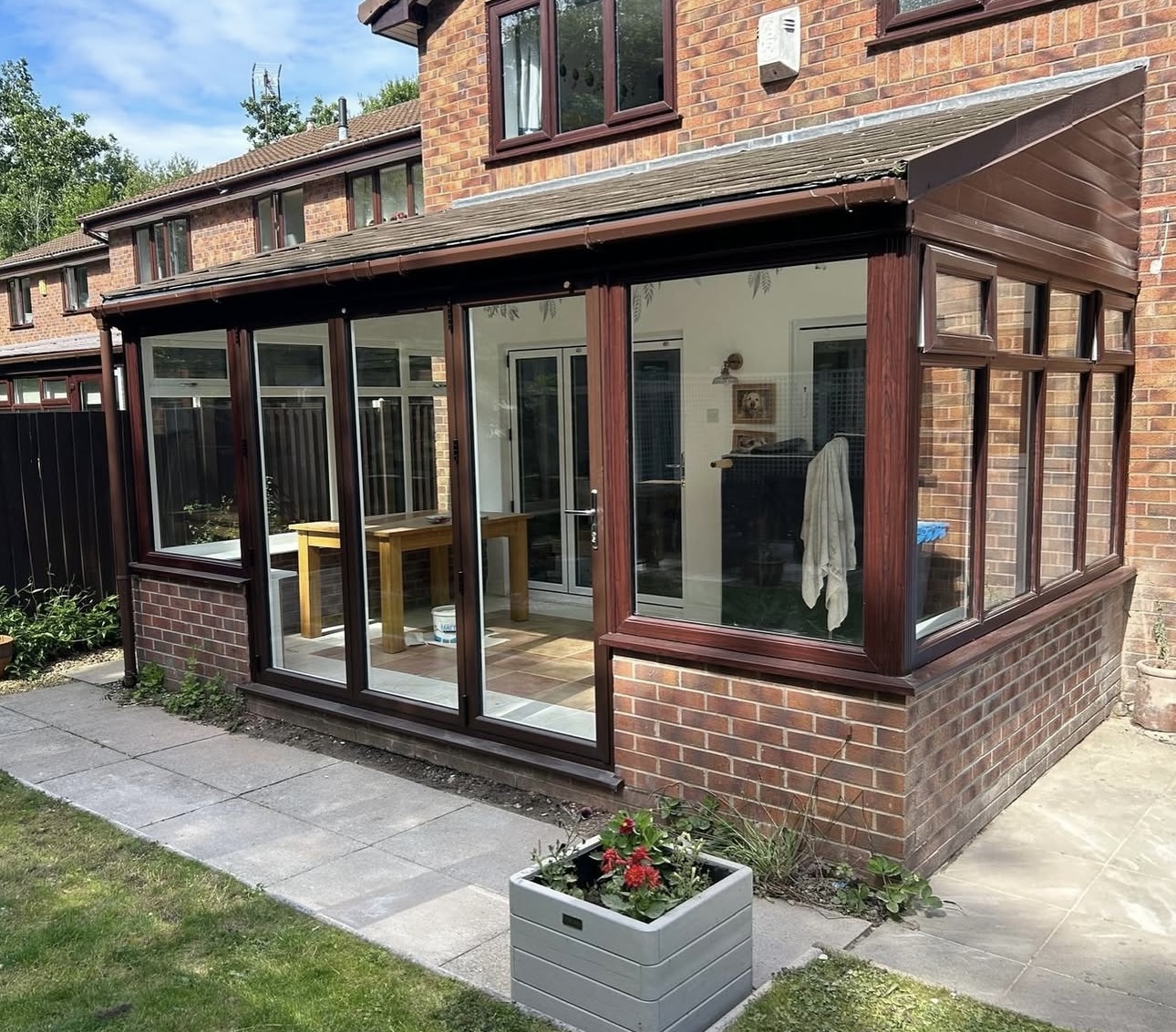 A brick home with a glass extension and dark-framed doors opening onto a paved patio