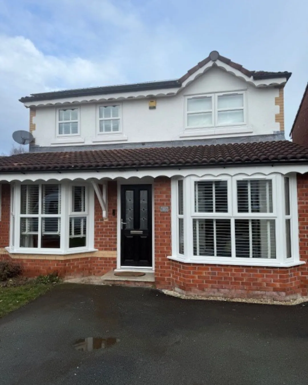 Two-story home with white bay windows, a white rendered upper floor and a black front door with glazed panels