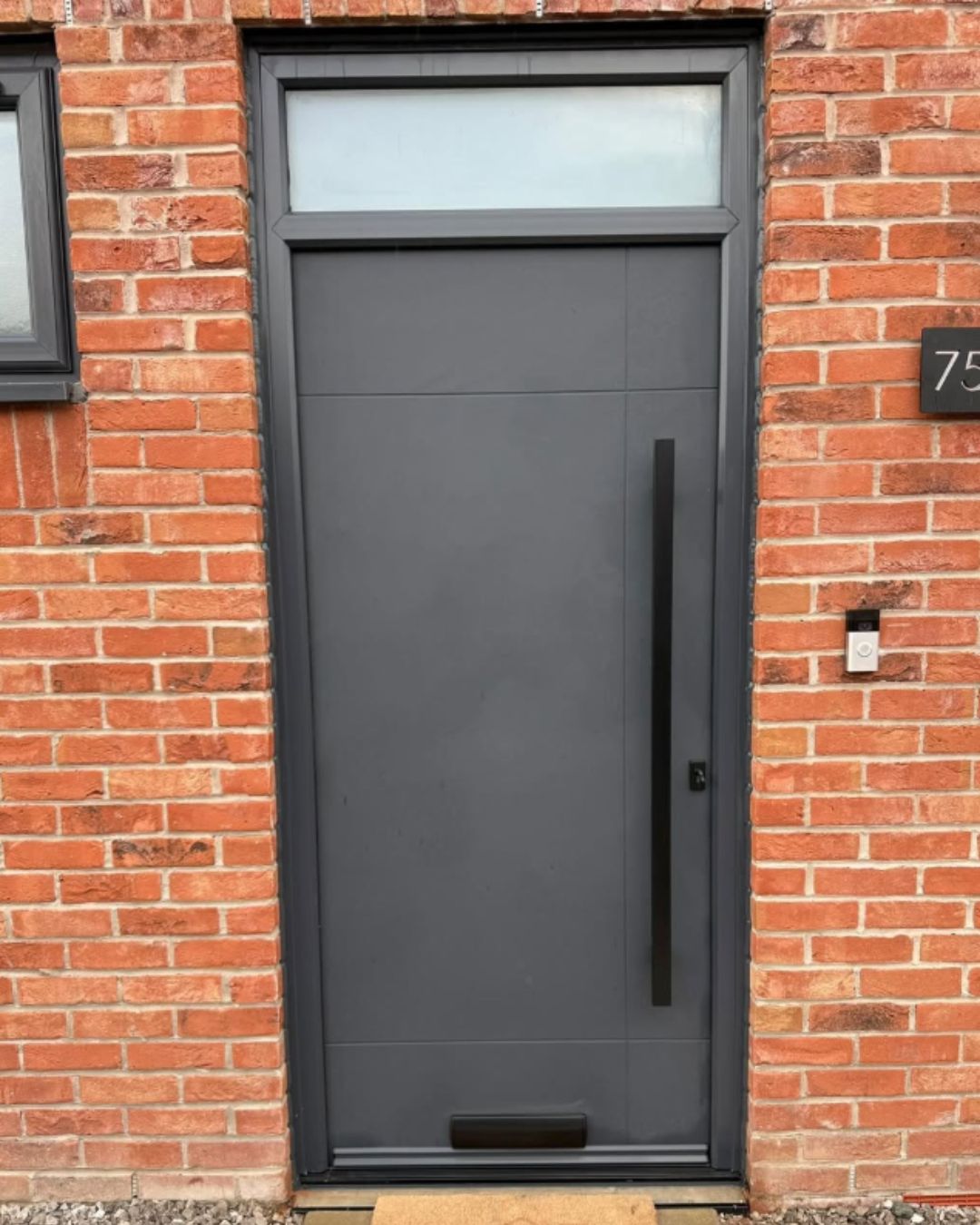 Anthracite grey front door with a matching glazed transom above, set in a red brick wall