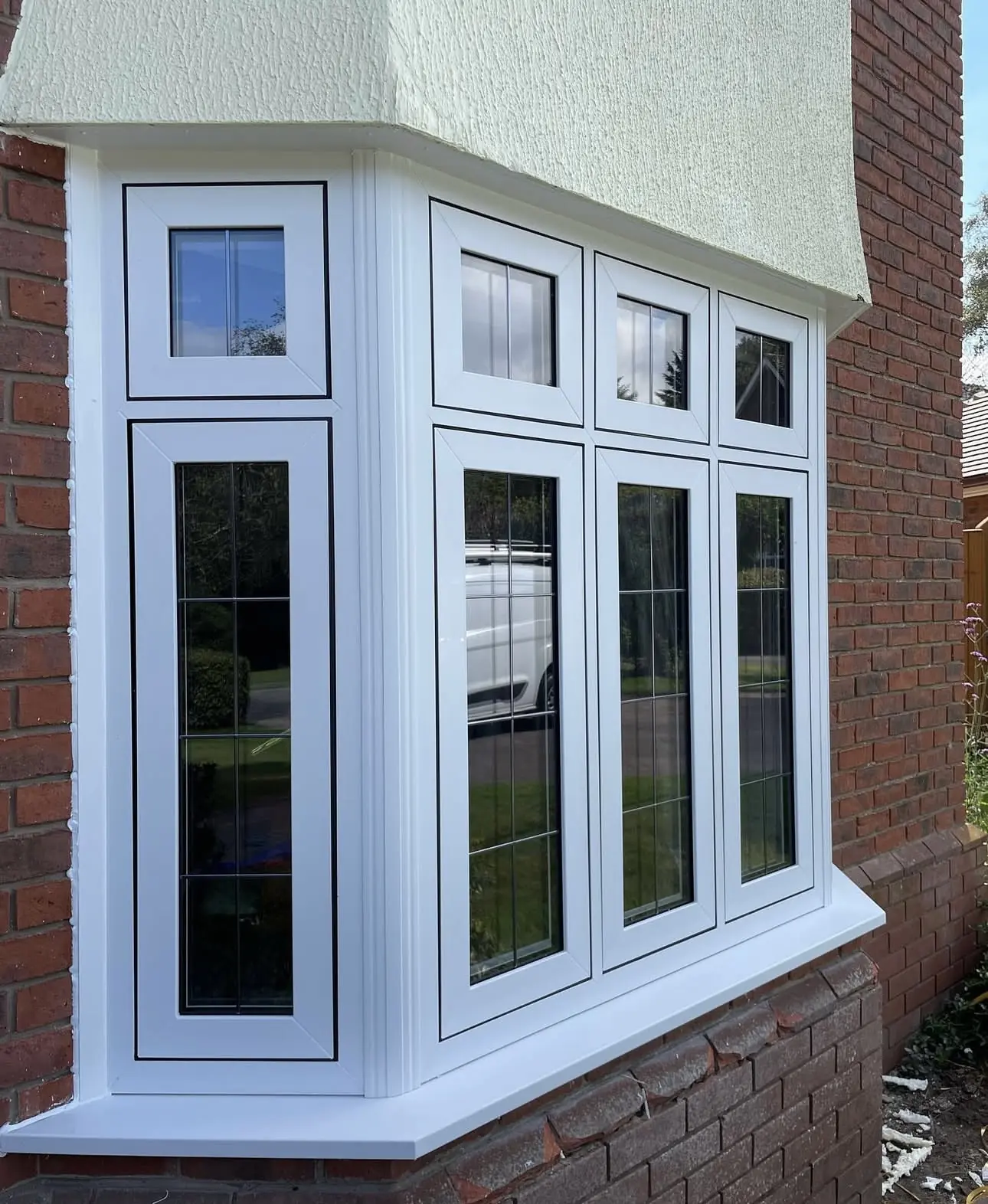 White bay window with decorative leaded glass bars on a red brick and cream rendered home